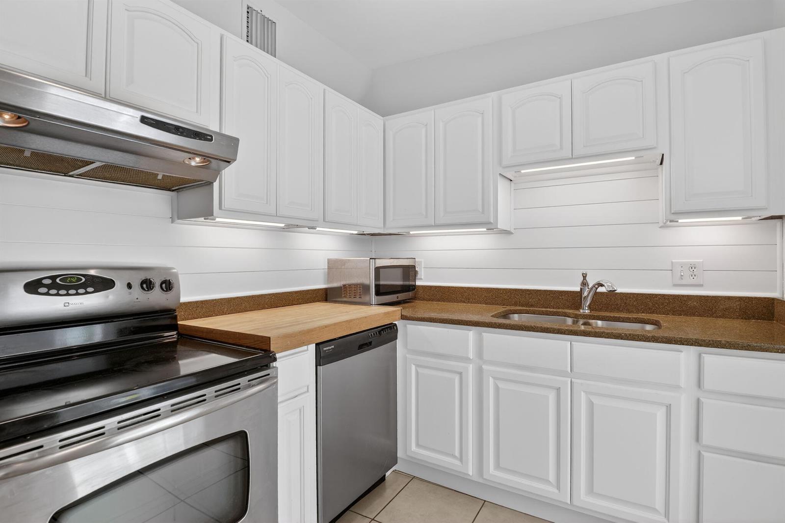 A kitchen features white cabinets, stainless steel appliances, a wood countertop, and a brown backsplash — 1932 Cedarwood Drive, Melbourne FL 32935, MELBOURNE, FL