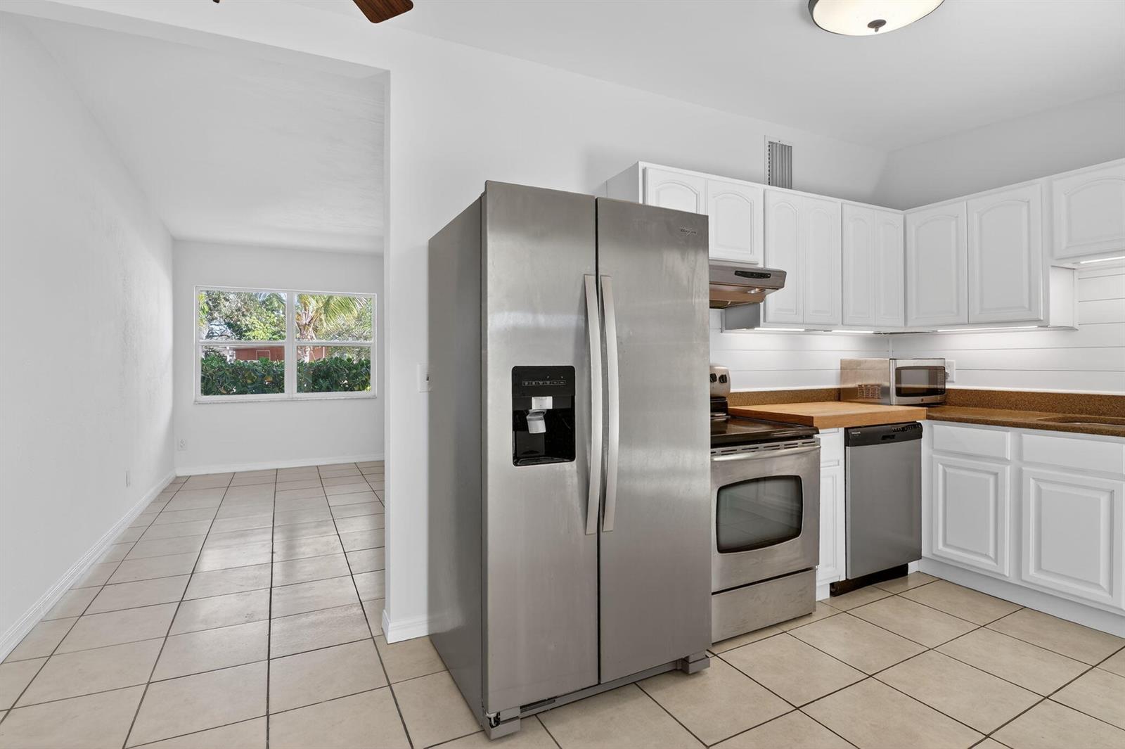 A kitchen with stainless steel appliances, white cabinets, and tile flooring opens to a dining area — 1932 Cedarwood Drive, Melbourne FL 32935, MELBOURNE, FL