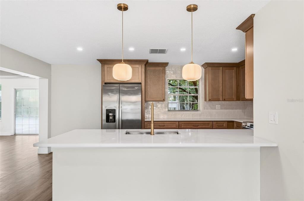 A kitchen features a white island, stainless steel refrigerator, wood cabinets, and two pendant lights — 17901 PALM STREET, UMATILLA, FL