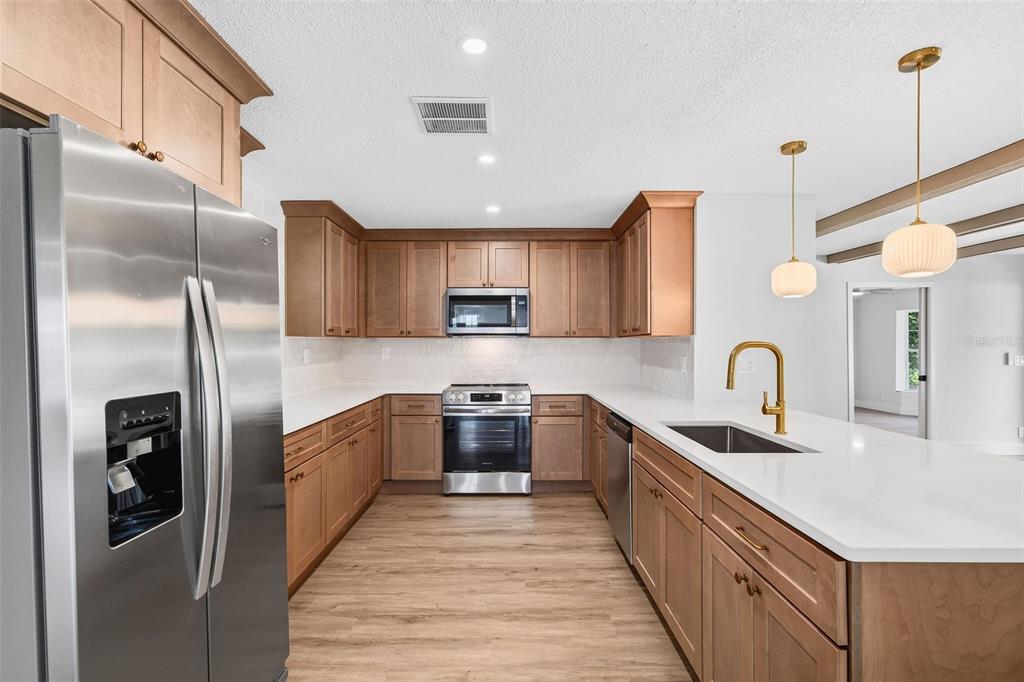 A modern kitchen features light wood cabinets, white countertops, stainless steel appliances, and gold fixtures — 17901 PALM STREET, UMATILLA, FL