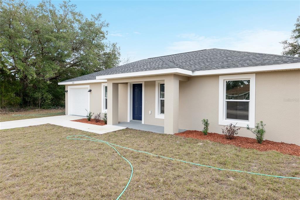 A single-story house with a tan stucco exterior, a dark blue front door, and a garage — 24035 NW AMBERJACK AVENUE, DUNNELLON, FL