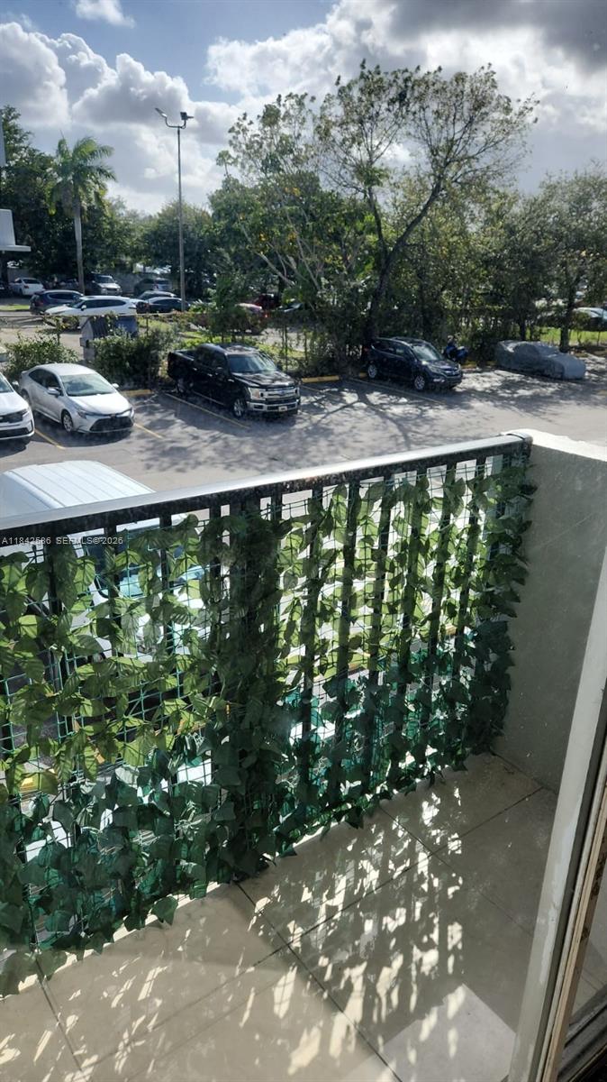 A balcony with a privacy screen of artificial ivy overlooks a parking lot with cars — 16450 NW 2nd Ave # 206, Miami FL 33169, MIAMI, FL