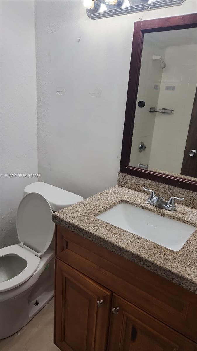 A bathroom features a granite-topped vanity with a wooden cabinet, a mirror, and a toilet — 16450 NW 2nd Ave # 206, Miami FL 33169, MIAMI, FL