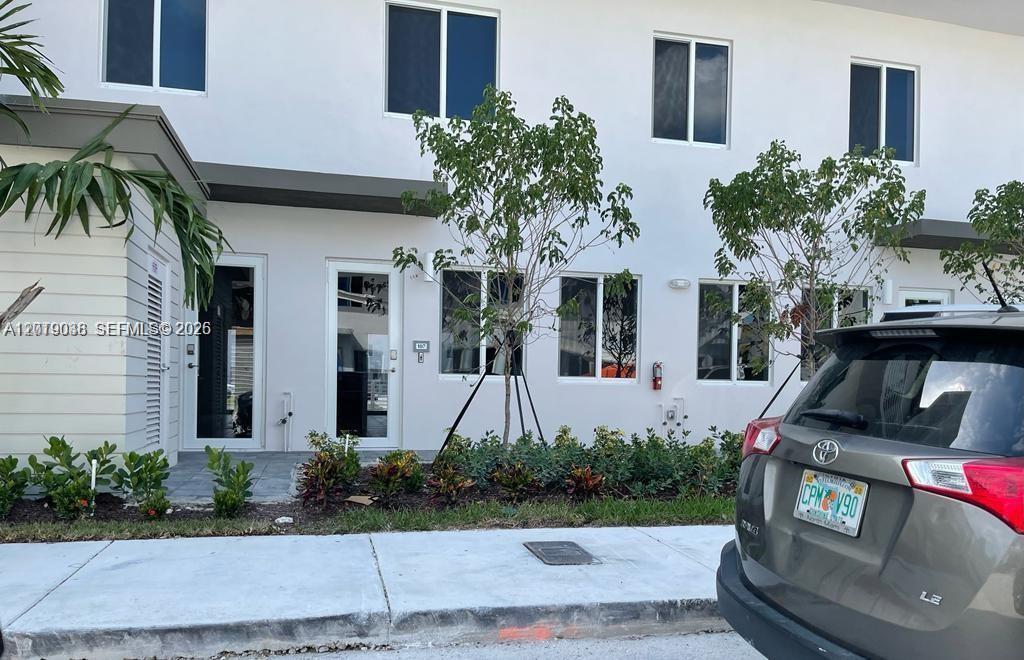 A modern two-story townhouse exterior with white walls, glass doors, and a parked SUV — DORAL, FL