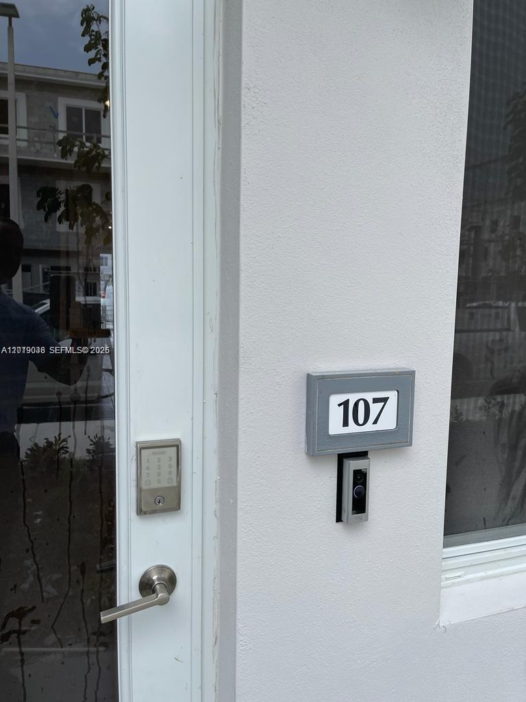 A white door with a digital keypad and a doorbell camera is labeled with the number 107 — DORAL, FL