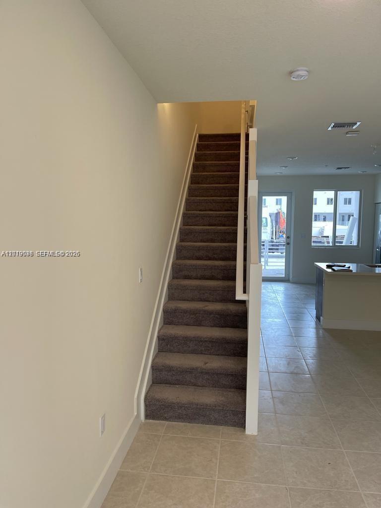 A carpeted staircase leads to an upper floor next to a tiled kitchen area — DORAL, FL