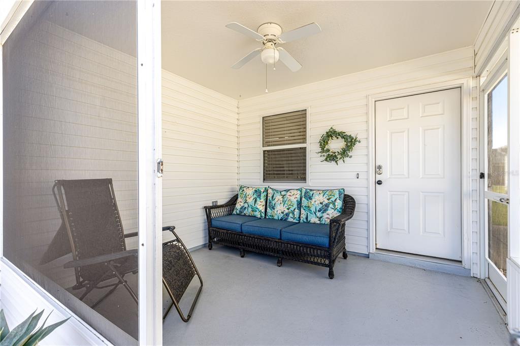 A screened-in porch features a wicker sofa with floral cushions, a ceiling fan, and white siding — 2140 ESTEVEZ DRIVE, LADY LAKE, FL