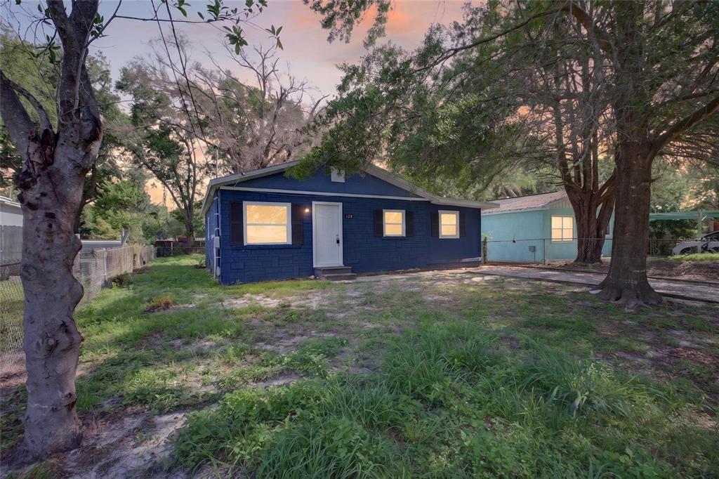 A blue single-story house with a white door sits on a grassy lot with trees — 128 E 145TH AVENUE, TAMPA, FL