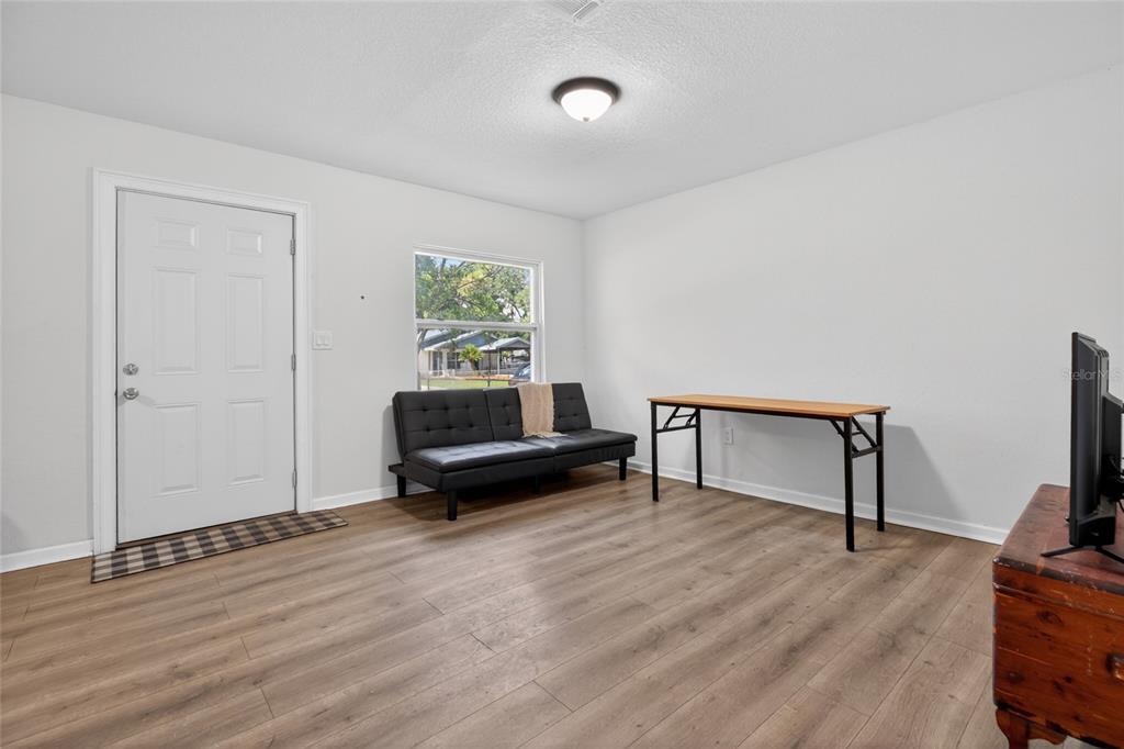 A room with light-colored walls, wood-look flooring, a black futon, and a folding table — 128 E 145TH AVENUE, TAMPA, FL