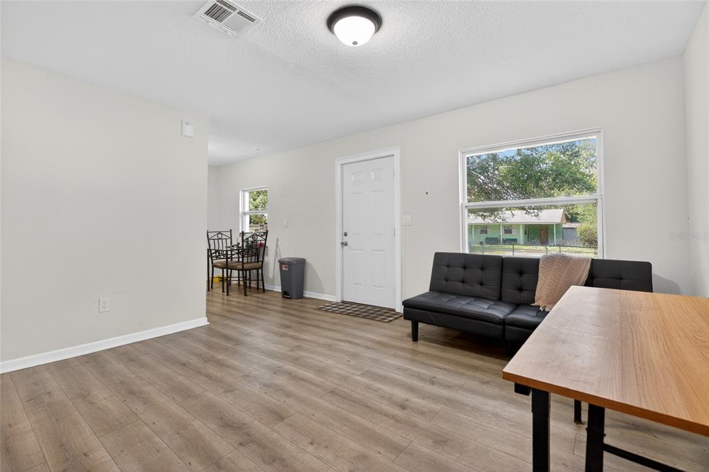 A living room with light wood-look flooring, a black futon, and a white entry door — 128 E 145TH AVENUE, TAMPA, FL