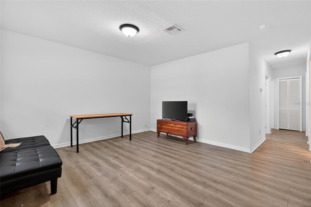 A living room features light wood-look flooring, white walls, a black futon, and a television — 128 E 145TH AVENUE, TAMPA, FL
