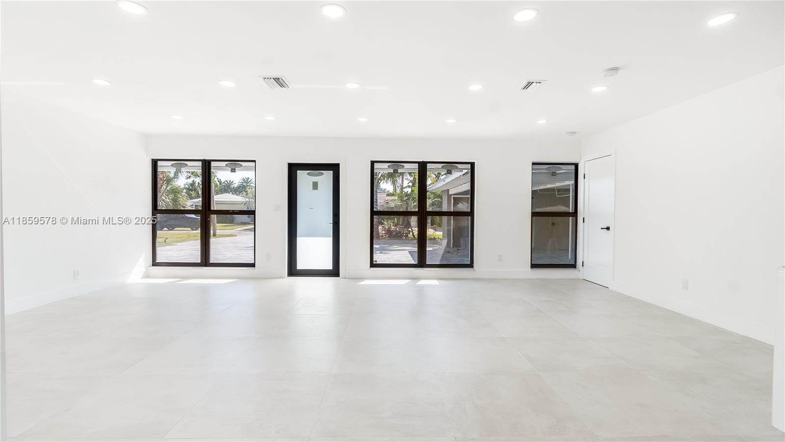 A bright, minimalist room features white walls, large windows, a glass door, and tiled flooring — 2417 NE 18th Ave, Wilton Manors FL 33305, WILTON MANORS, FL