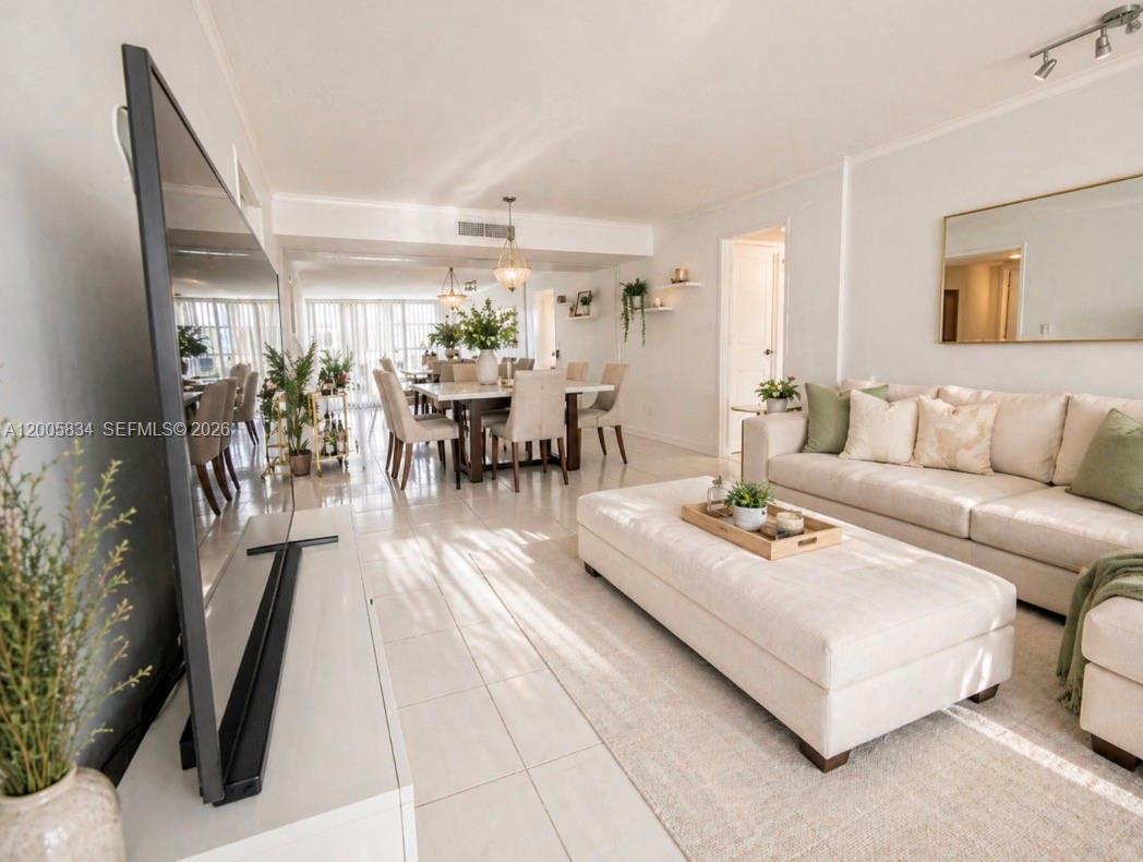 A bright living and dining area features white tile floors, neutral furniture, and large windows — 701 Three Islands Blvd # 120, Hallandale Beach FL 33009, HALLANDALE BEACH, FL