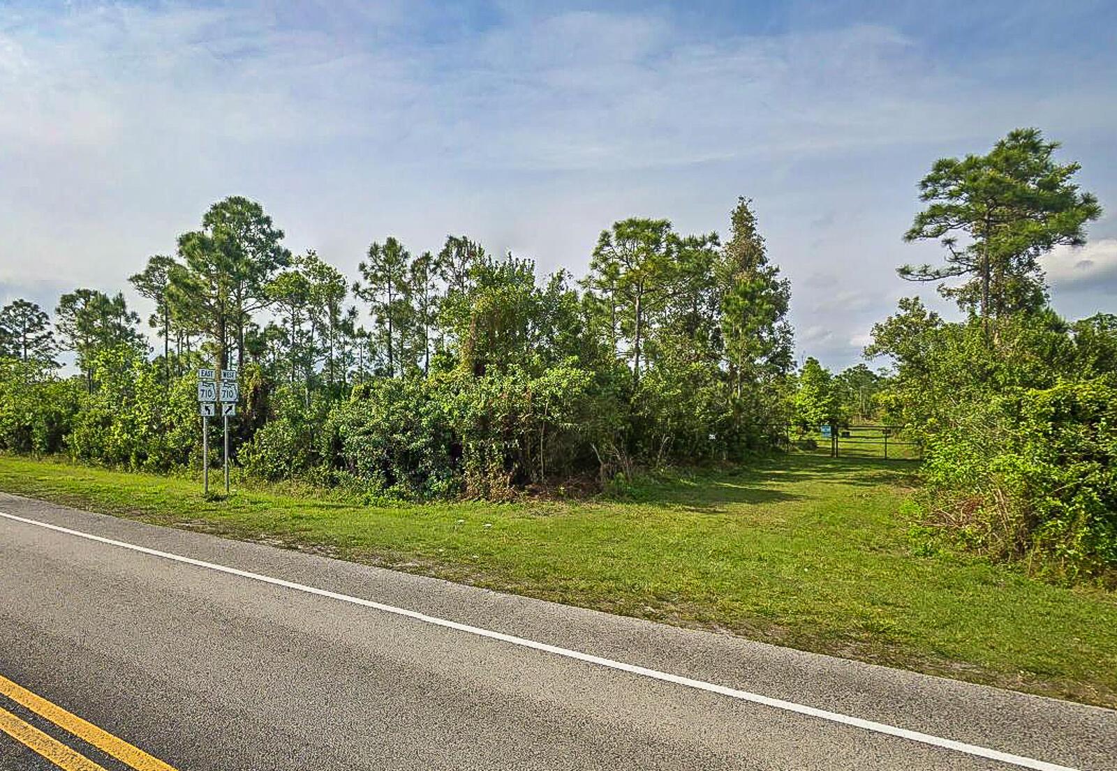 A grassy lot with trees and shrubs sits beside a paved road with highway signs — 19791 Indiantown Road, Jupiter FL 33478, JUPITER, FL