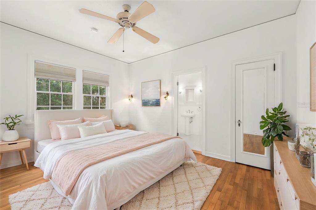 A bright bedroom features a bed with pink bedding, hardwood floors, and an attached bathroom — 717 NE BOULEVARD, GAINESVILLE, FL