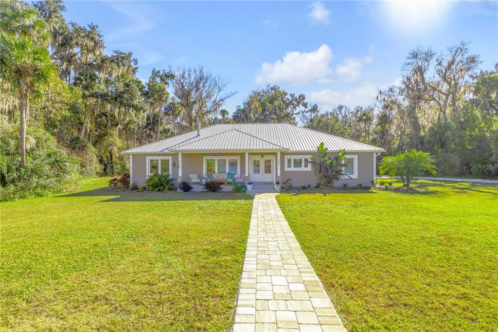 A single-story house with a metal roof and a stone walkway sits on a lawn — 2760 PEARL LAKE TRAIL, NEW SMYRNA BEACH, FL