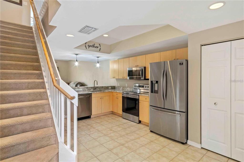 A carpeted staircase leads upward next to a kitchen with light wood cabinets and tile flooring — 1186 RIO DE JANEIRO AVENUE UNIT 104, PUNTA GORDA, FL