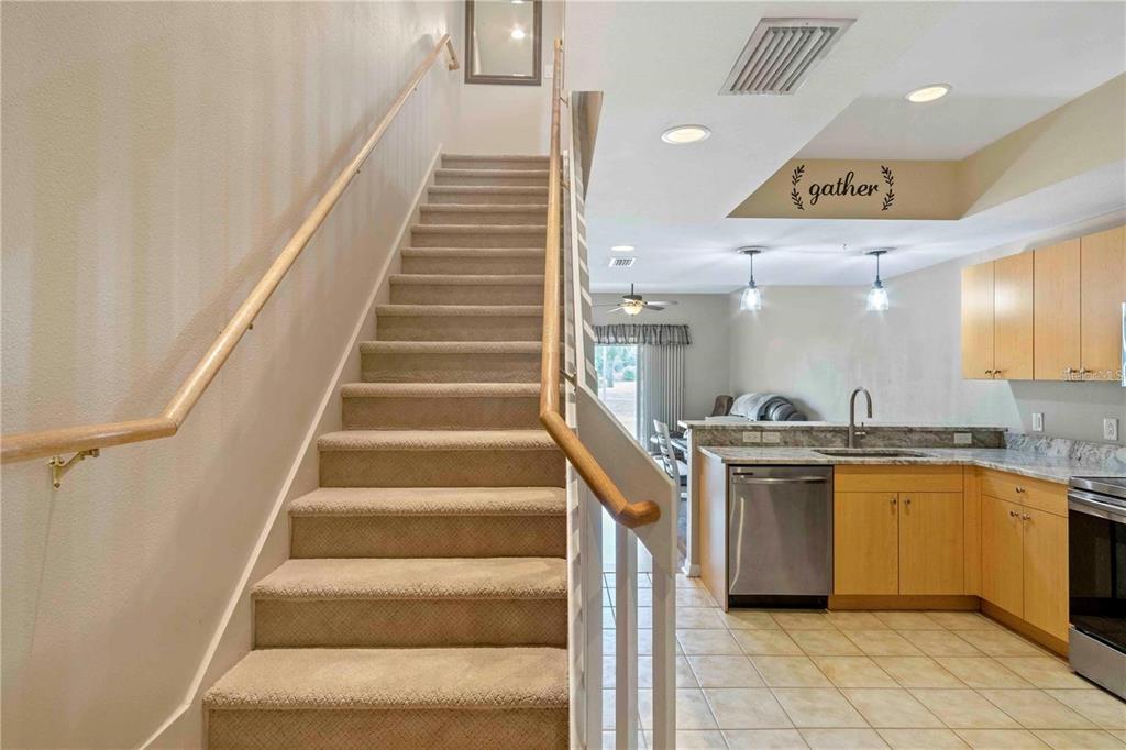 A kitchen with light wood cabinets and tile flooring sits beside a carpeted staircase — 1186 RIO DE JANEIRO AVENUE UNIT 104, PUNTA GORDA, FL