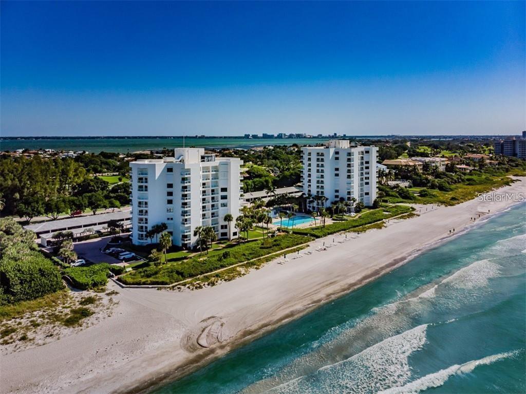 An aerial view shows two white high-rise condominium buildings situated along a sandy beach — 1050 LONGBOAT CLUB ROAD UNIT 804, LONGBOAT KEY, FL