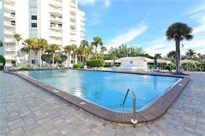 A rectangular swimming pool sits on a paved patio in front of a tall apartment building — 1050 LONGBOAT CLUB ROAD UNIT 804, LONGBOAT KEY, FL