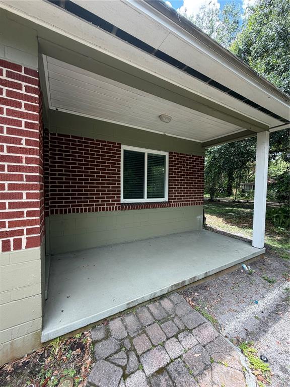 A covered concrete porch features a brick wall, a single window, and a wooden post — 1120 PALMER STREET, ORLANDO, FL