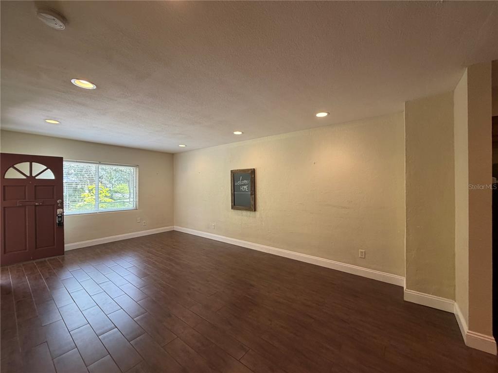 A living room with dark wood-look tile flooring, recessed lighting, and a front door — 1120 PALMER STREET, ORLANDO, FL