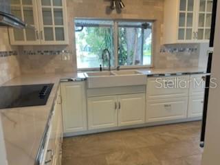 A kitchen features white cabinets, a farmhouse sink, stone countertops, and a window overlooking greenery — 3601 LANDALE DRIVE, HOLIDAY, FL