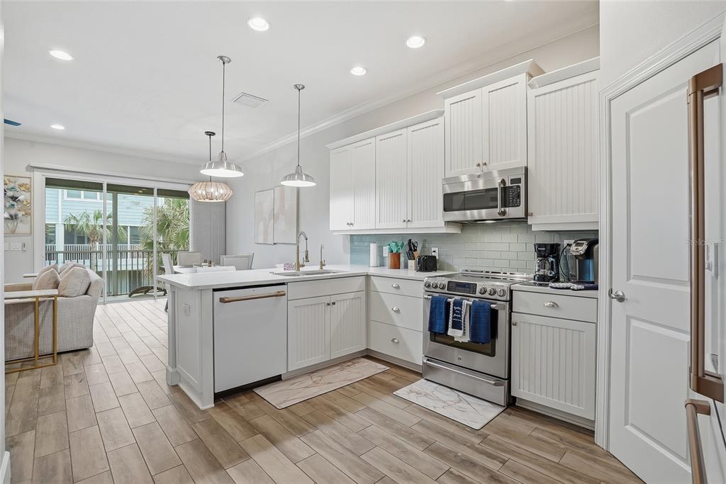 A modern kitchen features white cabinetry, stainless steel appliances, and a light-colored tile floor — 3162 MOORINGS DRIVE, ST PETERSBURG, FL