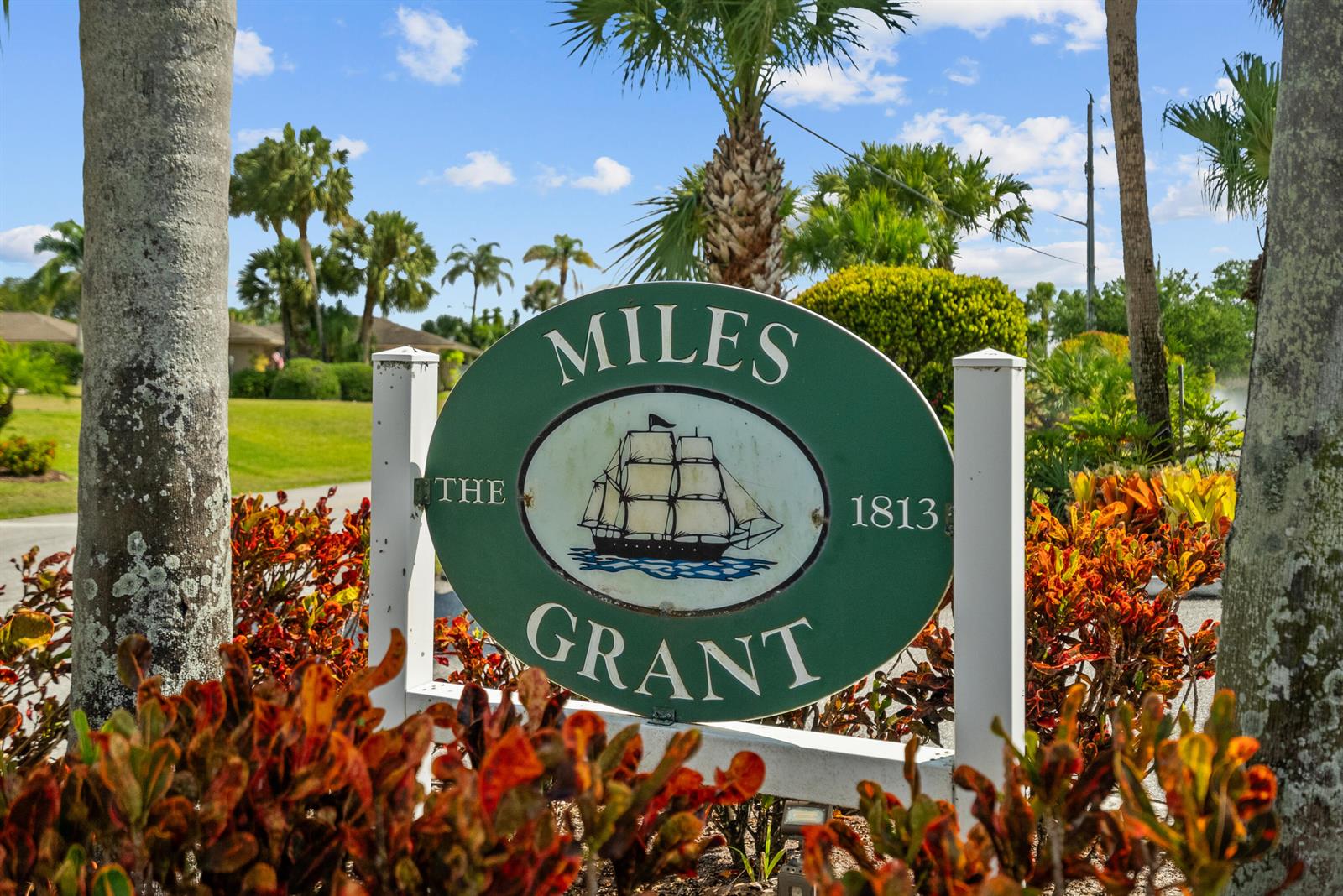 A green oval sign for Miles Grant with a ship illustration stands outdoors among plants — 5393 SE Miles Grant Road SE # 202, Stuart FL 34997, STUART, FL