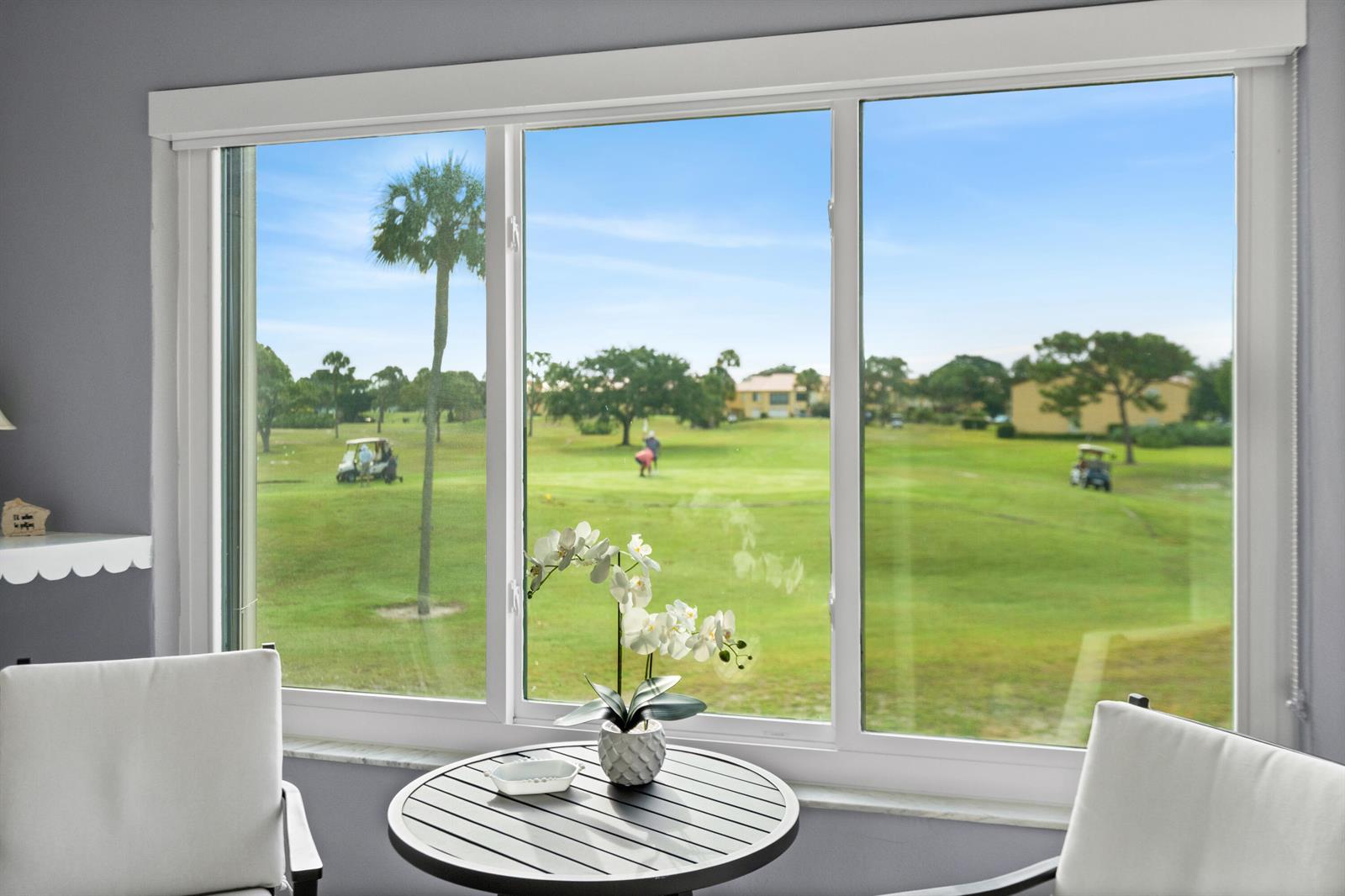 A view of a golf course through a large window behind a small table — 5393 SE Miles Grant Road SE # 202, Stuart FL 34997, STUART, FL