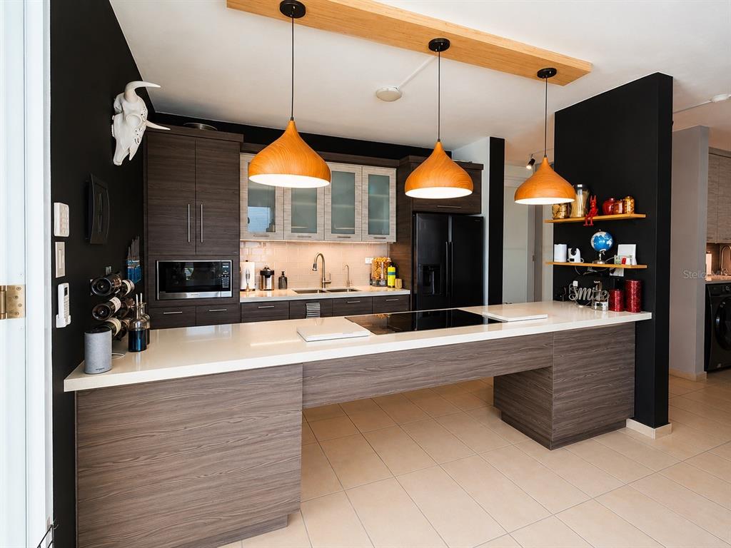 A modern kitchen features dark wood cabinetry, a white countertop island, and three pendant lights — 1554 López Landron St. COND. CONDADO LES COURS UNIT PH 503, SAN JUAN, PR
