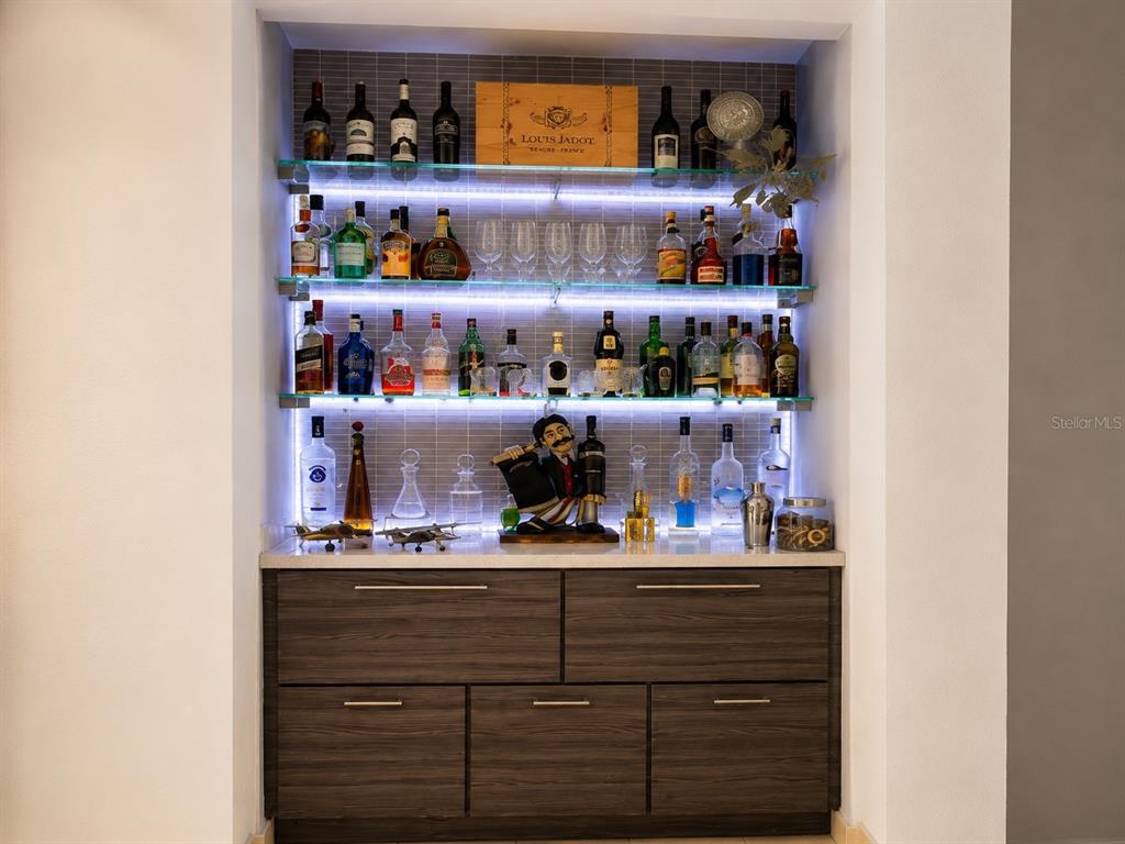 A home bar features illuminated glass shelves stocked with liquor bottles above dark wood cabinetry — 1554 López Landron St. COND. CONDADO LES COURS UNIT PH 503, SAN JUAN, PR