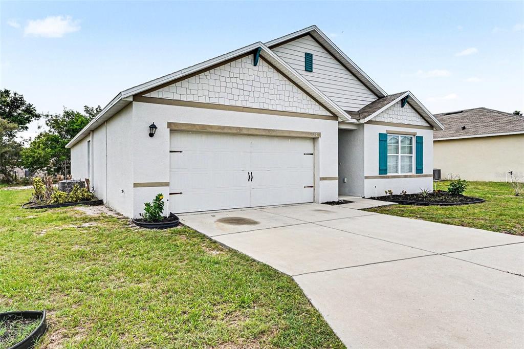 A single-story house with a two-car garage, light-colored stucco siding, and teal window shutters — 996 SUMMER GLEN DRIVE, WINTER HAVEN, FL