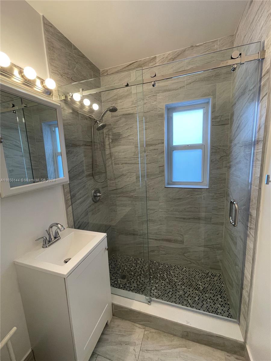 A bathroom features a white vanity, a glass-enclosed shower with pebble flooring, and tiled walls — 7710 NE 1st Ct, Miami FL 33138, MIAMI, FL