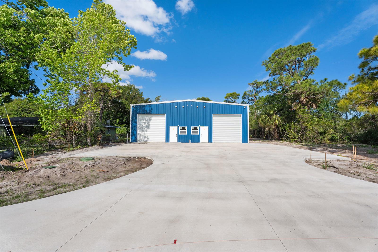 A blue metal warehouse building stands behind a large concrete driveway surrounded by trees — 2933 Harson Way, Fort Pierce FL 34946, FORT PIERCE, FL