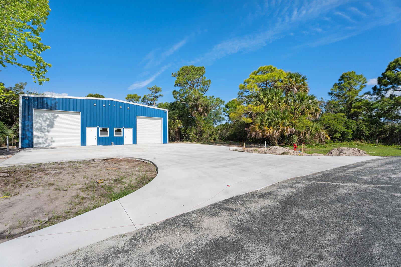 A blue metal warehouse building stands behind a large concrete driveway under a clear sky — 2933 Harson Way, Fort Pierce FL 34946, FORT PIERCE, FL