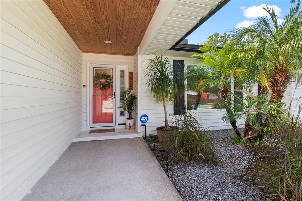 A concrete walkway leads to a front entrance with a red door and wood-paneled ceiling — 7905 55TH STREET E, PALMETTO, FL