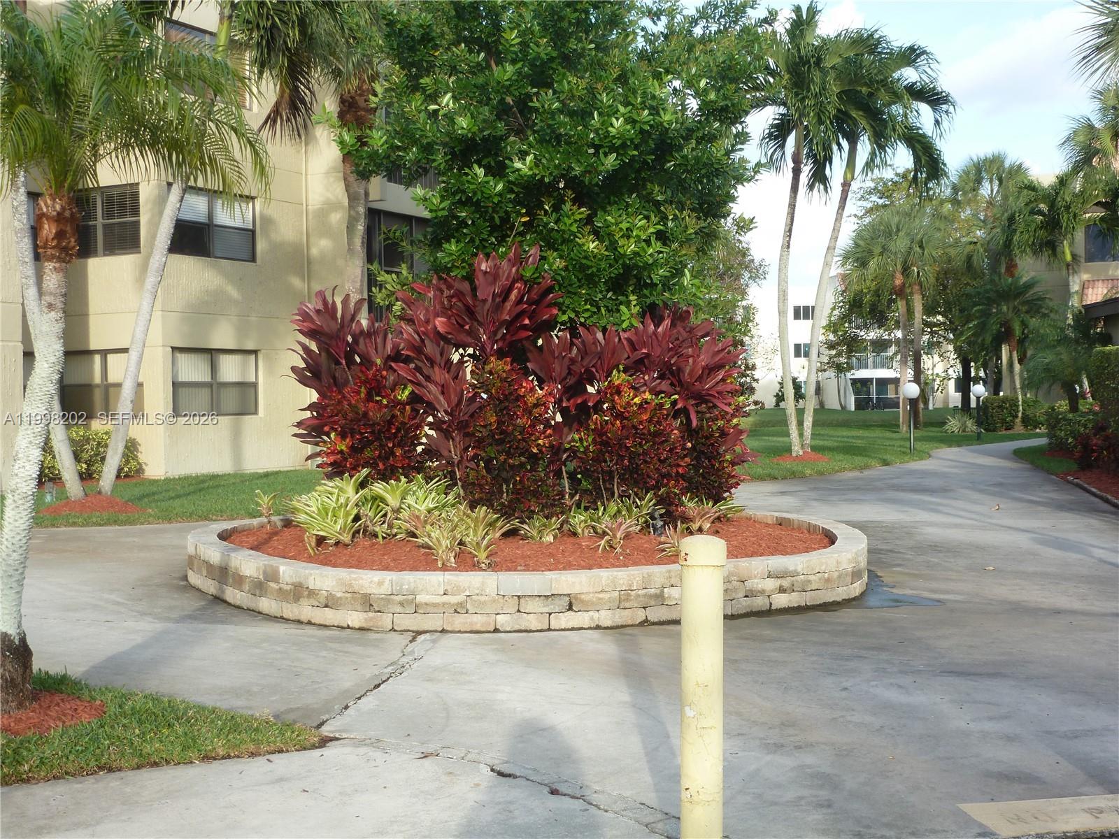 A circular stone planter filled with tropical plants sits in a paved courtyard — 220 Lakeview Dr # 301, Weston FL 33326, WESTON, FL