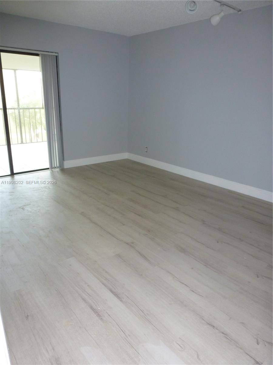 An empty room features light-colored wood-look flooring, gray walls, and a sliding glass door — 220 Lakeview Dr # 301, Weston FL 33326, WESTON, FL
