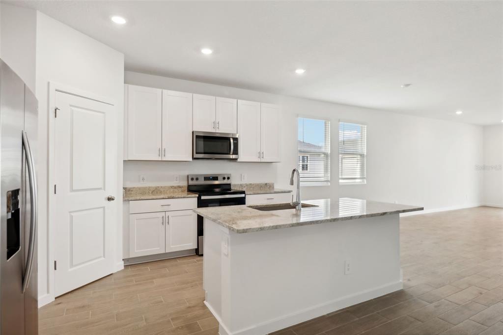 A kitchen with white cabinets, granite countertops, stainless steel appliances, and light wood-look flooring — 75 WANDERING CREEK WAY, PALM COAST, FL