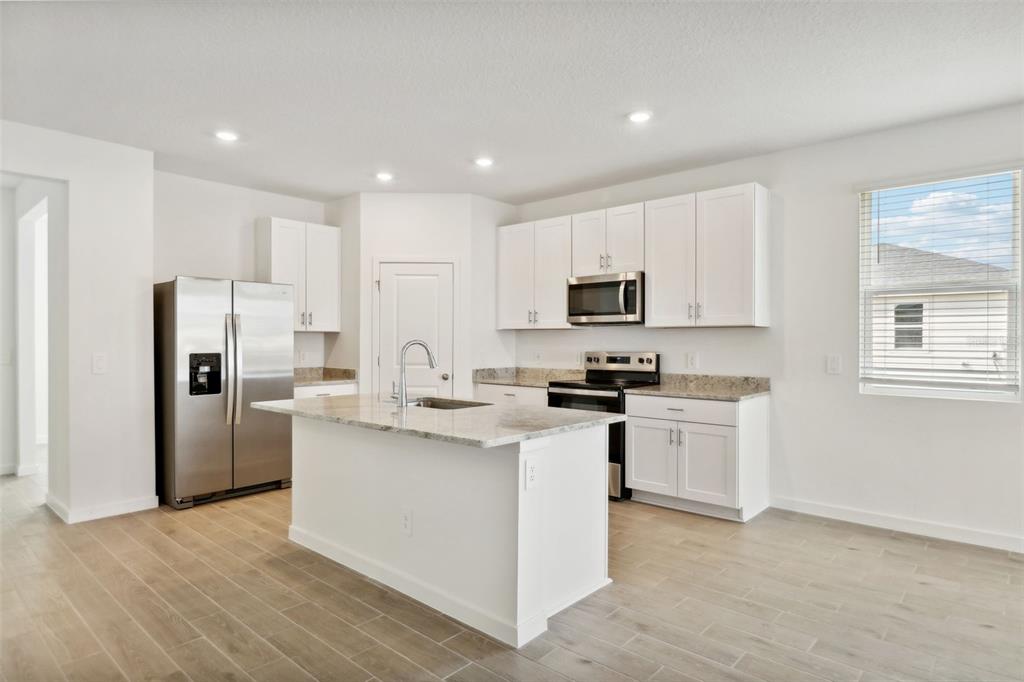 A modern kitchen features white cabinets, granite countertops, stainless steel appliances, and a central island — 75 WANDERING CREEK WAY, PALM COAST, FL
