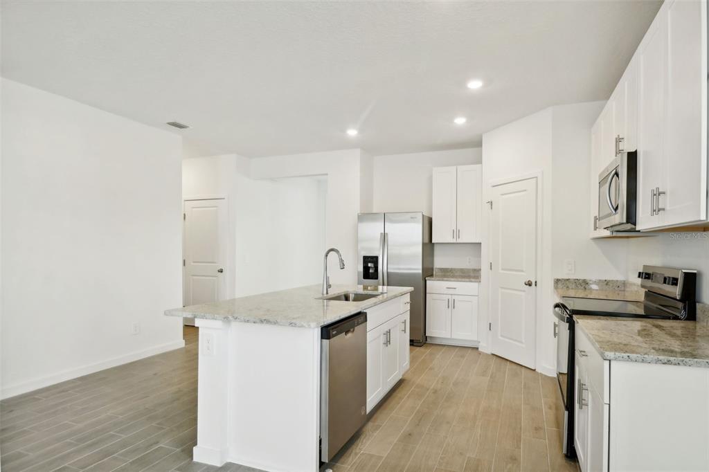 A kitchen with white cabinets, granite countertops, stainless steel appliances, and wood-look tile flooring — 75 WANDERING CREEK WAY, PALM COAST, FL