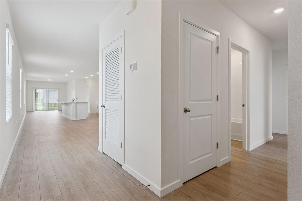 A hallway with light wood flooring leads to an open-concept kitchen and living area — 5198 BLANKET FLOWER STREET, APOPKA, FL