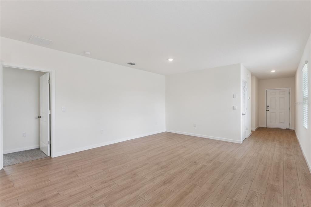 An empty living room features light wood-look flooring, white walls, and a front entry door — 5198 BLANKET FLOWER STREET, APOPKA, FL