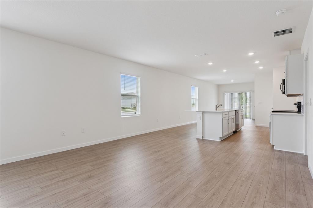 An open-concept living area features light wood-look flooring, white walls, and a modern kitchen island — 5198 BLANKET FLOWER STREET, APOPKA, FL