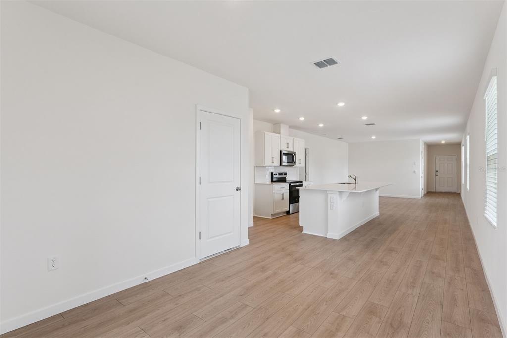 An open-concept kitchen and living area features white cabinetry, a central island, and wood-look flooring — 5198 BLANKET FLOWER STREET, APOPKA, FL
