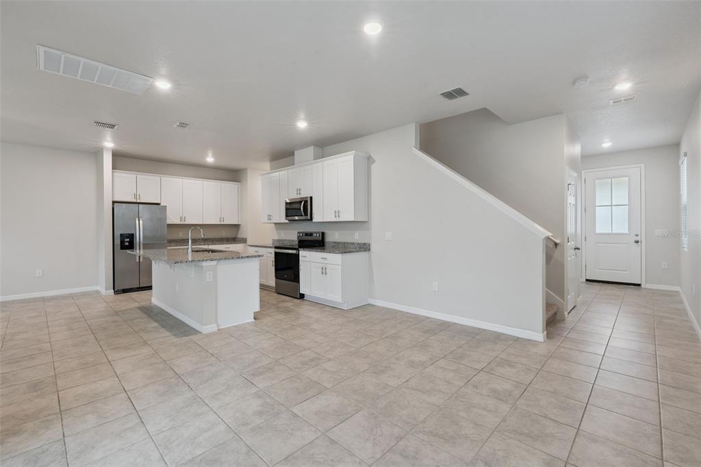 A kitchen with white cabinets, granite countertops, and tile flooring opens to a staircase area — 2292 MYSTIC MAZE LANE, CLERMONT, FL