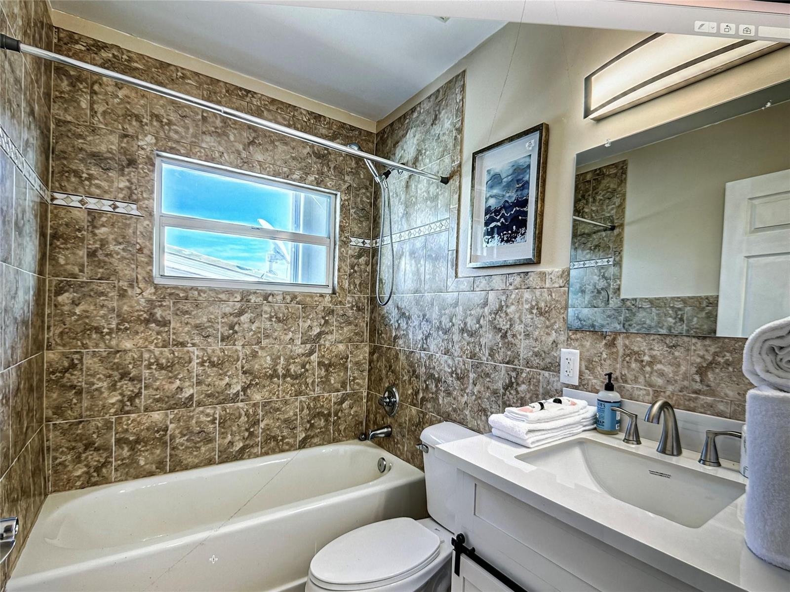 A bathroom features a white vanity, a toilet, and a bathtub with brown tiled walls — 141 Rutland Boulevard, West Palm Beach FL 33405, WEST PALM BEACH, FL
