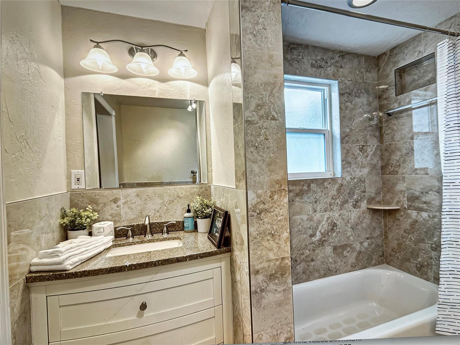 A bathroom features a white vanity with a granite countertop and a tiled shower-tub combo — 141 Rutland Boulevard, West Palm Beach FL 33405, WEST PALM BEACH, FL