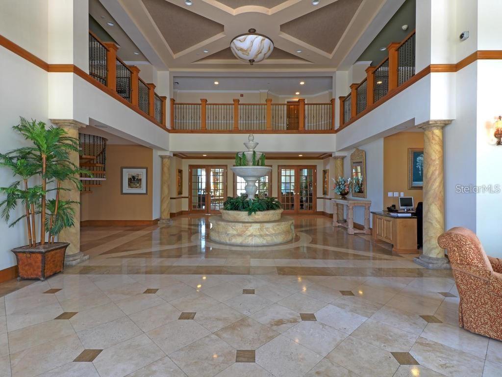 A grand lobby features a central tiered fountain, marble floors, and a mezzanine balcony — 1170 GULF BOULEVARD UNIT 1803, CLEARWATER BEACH, FL